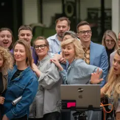 Grupa ludzi śmieje się i pozuje do zdjęcia, jakby przygotowywali się do spektakli komediowych.