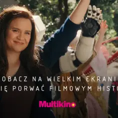 Uśmiechnięta kobieta z brązowymi włosami i osoba z protezą ręki na tle miasta.