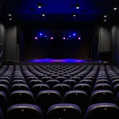 Puste rzędy foteli w ciemnej sali, gotowe na spektakl w Teatrze Muzycznym Praga. Niebieskie i różowe światła oświetlają scenę.