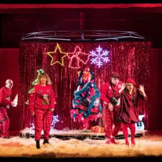 Scena teatralna z aktorami w świątecznych strojach, choinką i neonowymi ozdobami. Wesołe przedstawienia świąteczne dla dzieci.