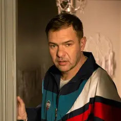 Tomasz Karolak w kolorowej kurtce, jakby wychodził zza drzwi. Może to scena z jednego z jego filmów?