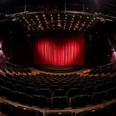 Pusta sala teatralna z czerwonymi kurtynami i rzędami czarnych foteli. Czekamy na spektakl z repertuaru Teatru Janda.