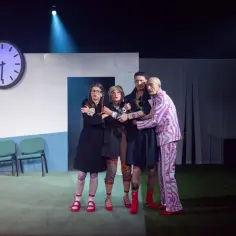 Cztery postacie na scenie, w tym jedna w piżamie w paski, przytulają się. Scenografia sugeruje nerwicę natręctw w teatrze.