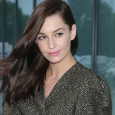 Agnieszka Więdłocha w błyszczącej sukience, znana z wielu filmów, seriali i programów, pozuje na tle nowoczesnego budynku.