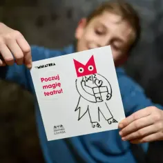Chłopiec trzyma kartkę z napisem "Poczuj magię teatru!". To zaproszenie na spektakl, idealne bilety do teatru dla dzieci.