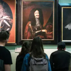 Zwiedzający podziwiają portrety w muzeum sztuki Wrocław. Widać barokowe stroje i peruki.