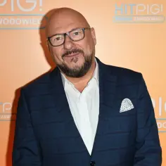 Piotr Gąsowski w garniturze, promujący swoje filmy. Uśmiechnięty, w okularach, na tle napisu "HITPIG!".