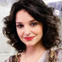 Uśmiechnięta Maria Dębska w stylizacji inspirowanej wężową skórą. Jej ciemne, kręcone włosy opadają na ramiona.