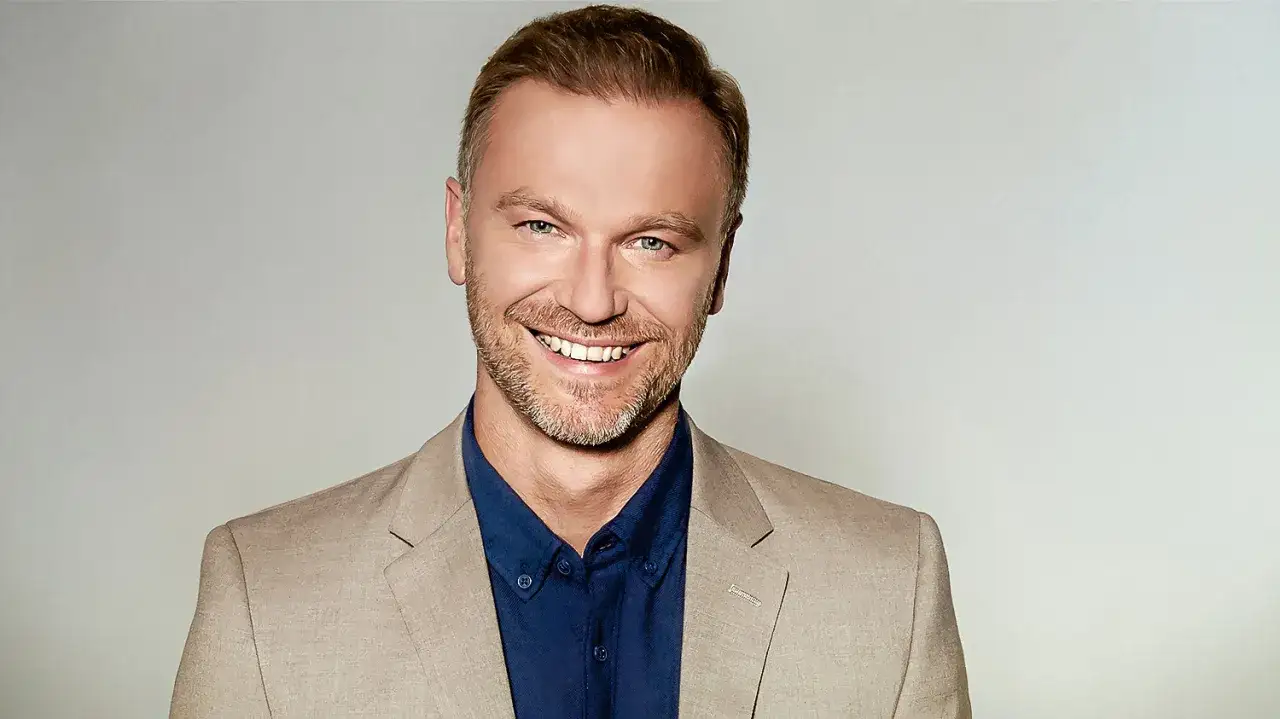 Uśmiechnięty Krystian Wieczorek w beżowej marynarce i granatowej koszuli, gotowy do kolejnych filmów.