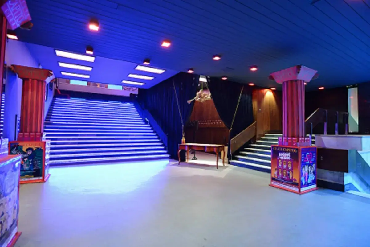 Wnętrze Teatru Capitol, gdzie niebieskie światła podkreślają schody i kolumny. Widać plakaty i stylowe meble.