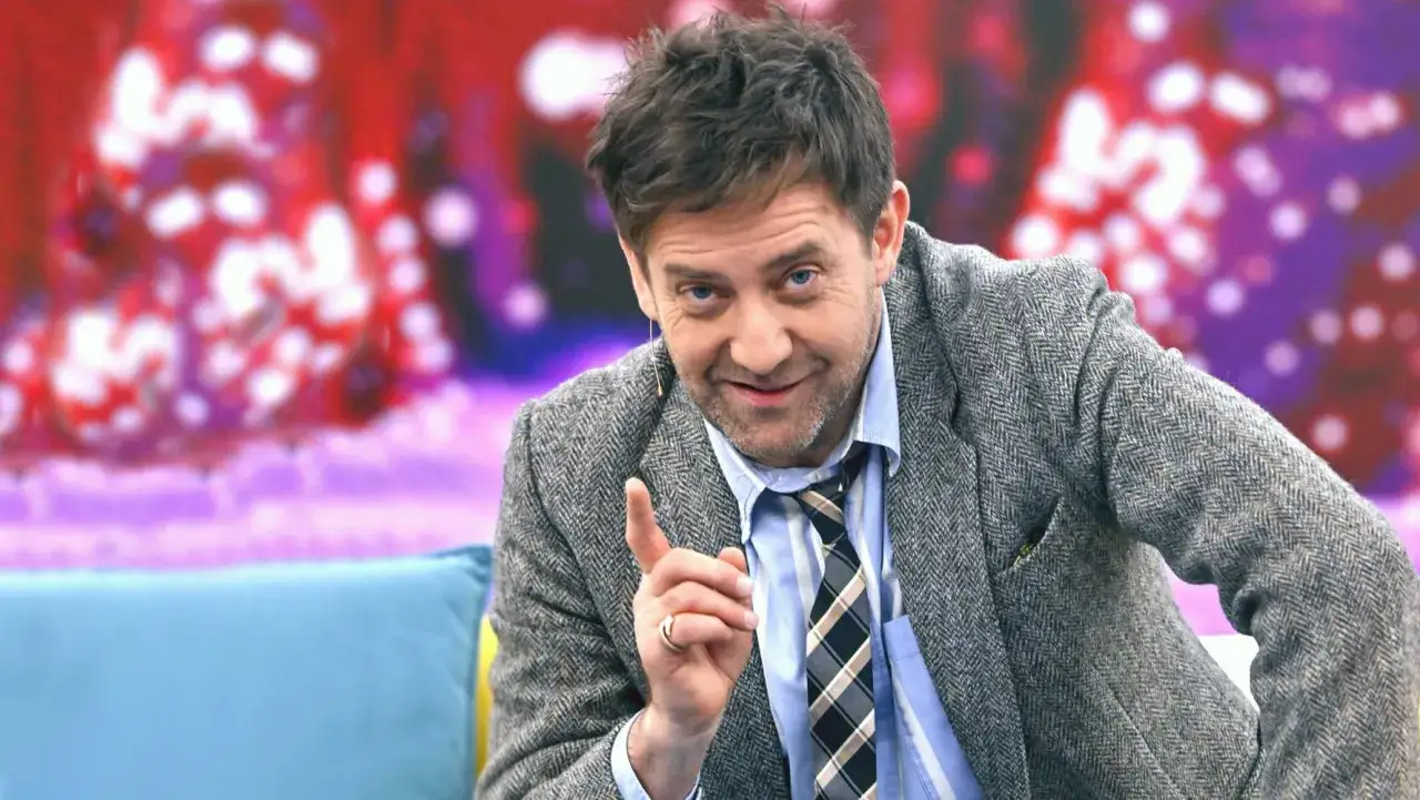 Rafał Królikowski w tweedowej marynarce, z charakterystycznym uśmiechem, jakby zapowiadał kolejny świetny z jego filmów.